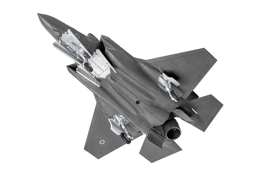 A high-angle view of an assembled and unpainted grey plastic model of an F-35B Lightning II fighter jet, showing the underside details.