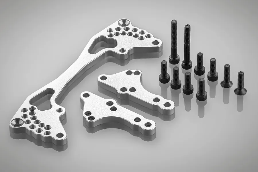 Rovan silver aluminium rear shock brace kit including three machined metal plates and a set of black steel screws on a grey background.
