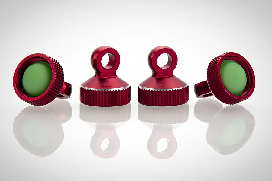 Four red anodized aluminium shock caps with green rubber seals, arranged on a white reflective surface.