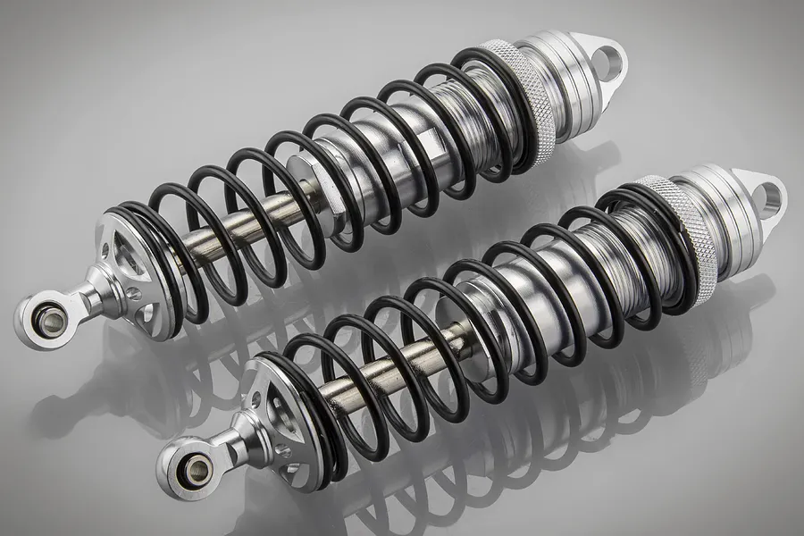 Two Rovan silver aluminium adjustable RC car shock absorbers with black springs on a grey reflective surface.
