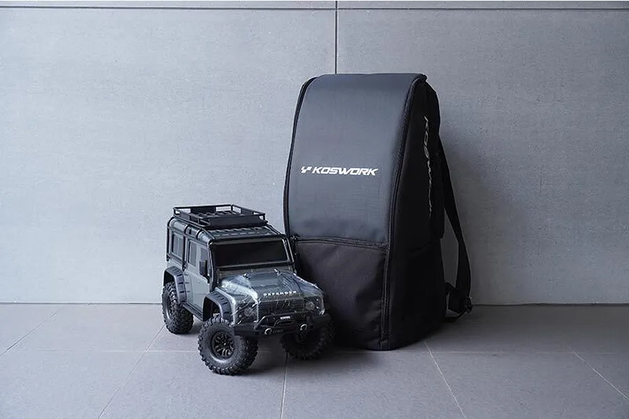 A black Koswork multi-function RC crawler backpack standing next to a 1/10 scale Land Rover Defender RC crawler on a grey tiled floor.