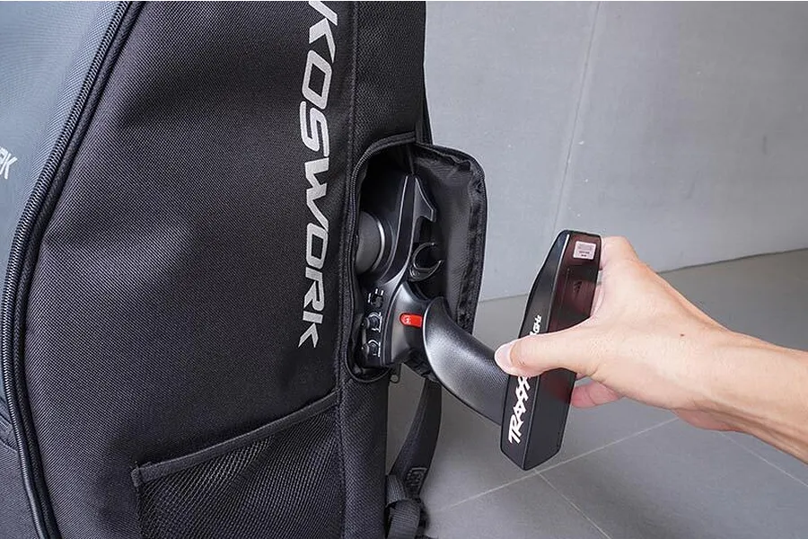 A person pulling a black Traxxas RC transmitter out of the side pocket of a black Koswork crawler backpack.