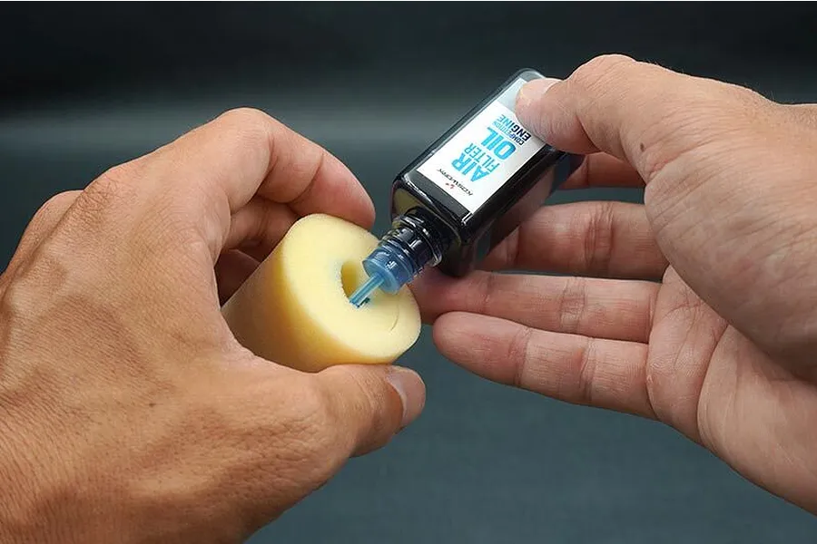 A person applying Koswork Competition Engine Air Filter Oil to a yellow foam RC air filter element.