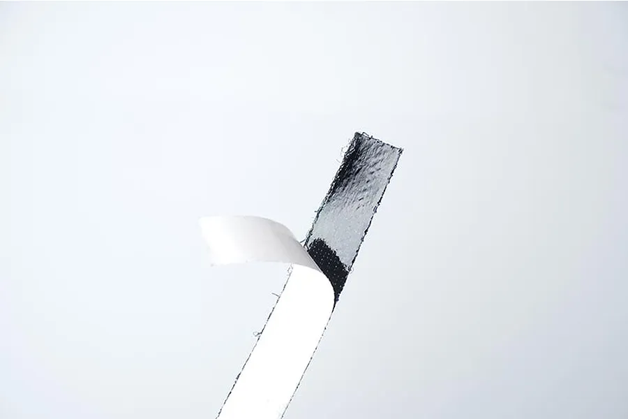 A strip of black adhesive hook and loop tape with a white paper backing partially peeled away against a white background.