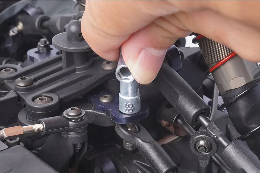 A hand using a silver metal nut wrench to tighten a nut on an RC car chassis.