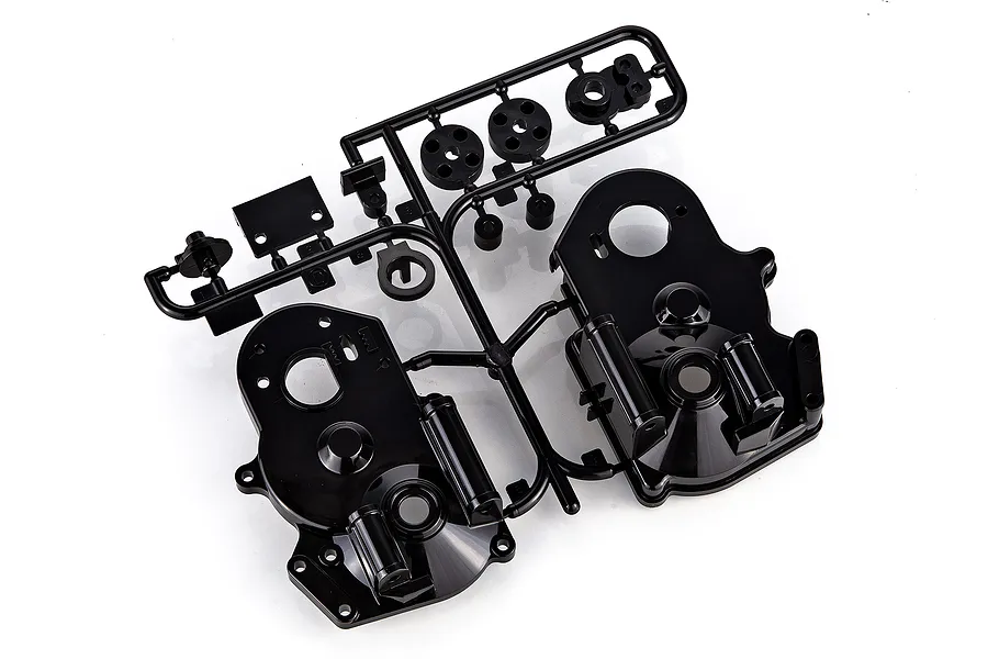 A black plastic Tamiya D parts sprue containing various RC car components, including gear covers and small circular parts, on a white background.