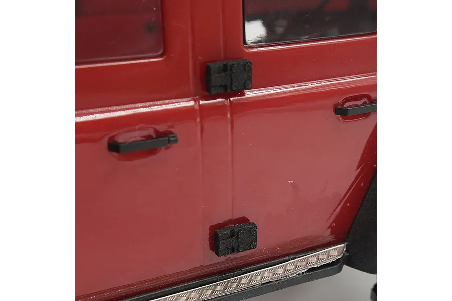 Close-up of a red RC car body showing black door hinges and door handles installed on the side panel.