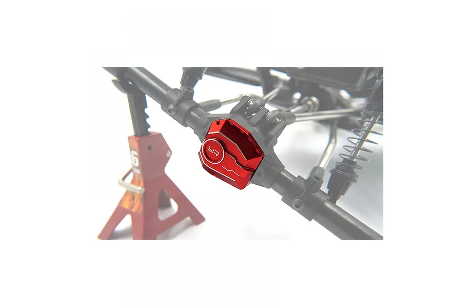 A red aluminium differential cover installed on an RC crawler axle, with a red jack stand in the background.