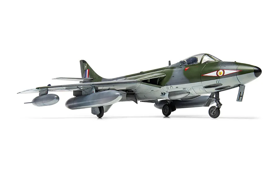 A completed 1/48 scale plastic model of a Hawker Hunter fighter jet, painted in green and grey camouflage with external fuel tanks, on a white background.