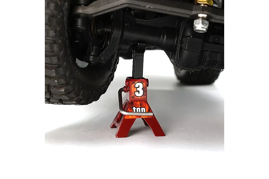 A red scale model jack stand supporting the axle of an RC vehicle against a white background.