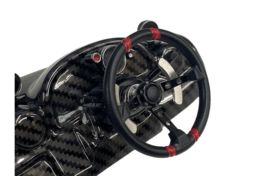 A detailed scale model RC car steering wheel and dashboard assembly featuring a carbon fiber pattern finish and red accents on the steering wheel rim.