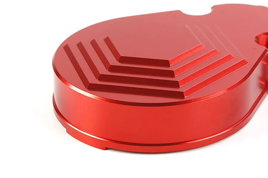 A close-up view of a red anodized aluminium transmission case for an RC car, featuring a stepped hexagonal design on its top surface.