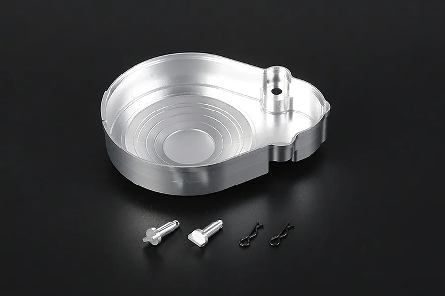 A silver aluminium transmission case component with two small metal pins and two black R-clips on a dark background.