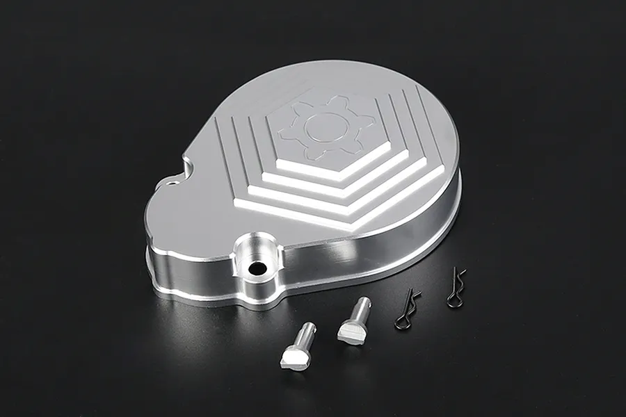 A silver aluminium RC transmission case with a gear-shaped design, accompanied by two metal pins and two black R-clips on a dark background.