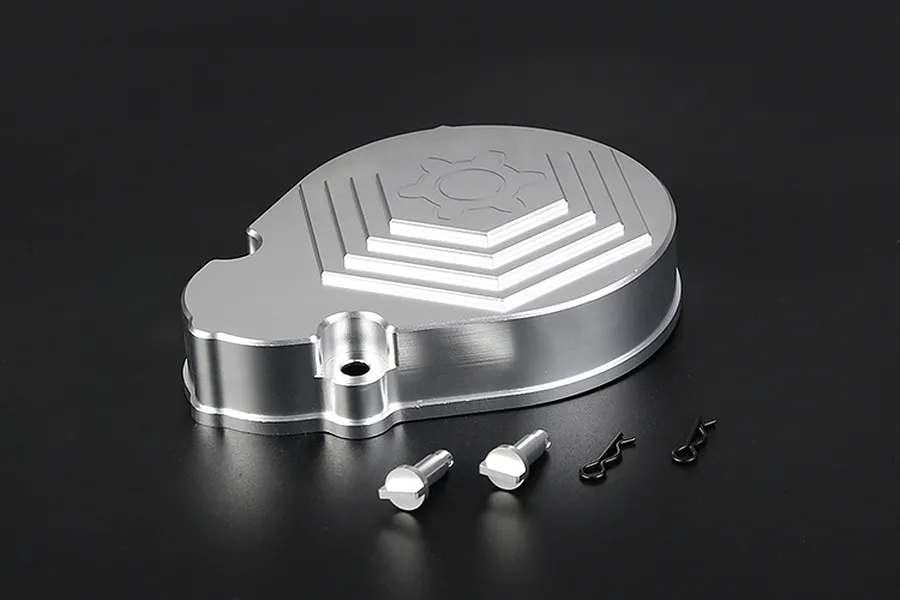 A silver aluminium RC transmission case with a gear-shaped design, accompanied by two metal pins and two black R-clips on a dark background.
