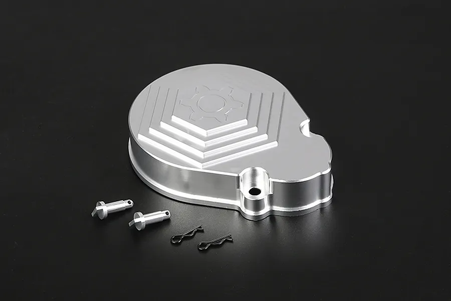 A silver aluminium transmission case cover with a gear logo engraving, accompanied by two small metal pins and two black R-clips on a black background.