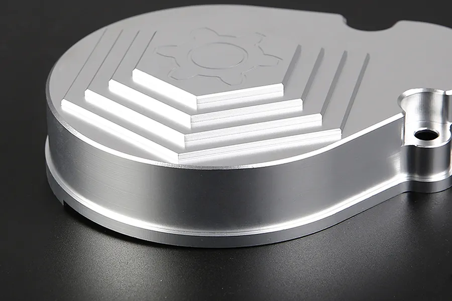 A silver aluminium Rovan transmission case with a machined gear logo on top, set against a dark background.