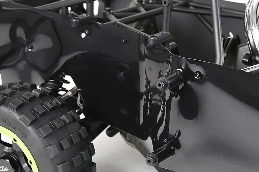 Close-up of a black plastic dust guard installed on the side of an RC buggy chassis, showing the mounting points and nearby off-road tire.