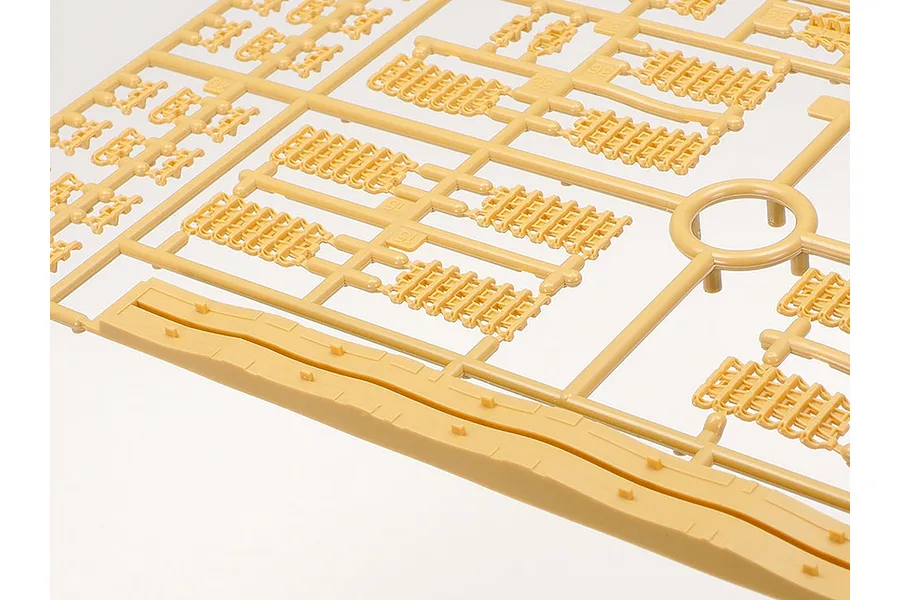 A close-up view of a tan plastic model kit sprue featuring various tank track link segments for a Tamiya military vehicle model.