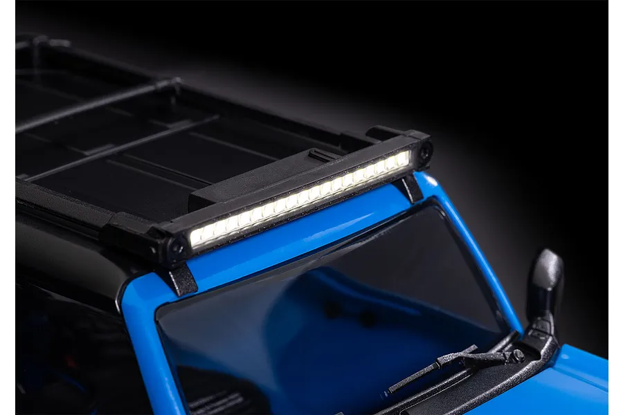 A bright LED light bar mounted to the roof rack of a blue RC crawler vehicle against a dark background.