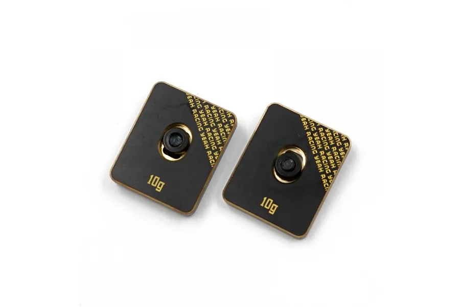Two rectangular Yeah Racing 10g brass chassis balancing weights with black coating and central mounting holes.