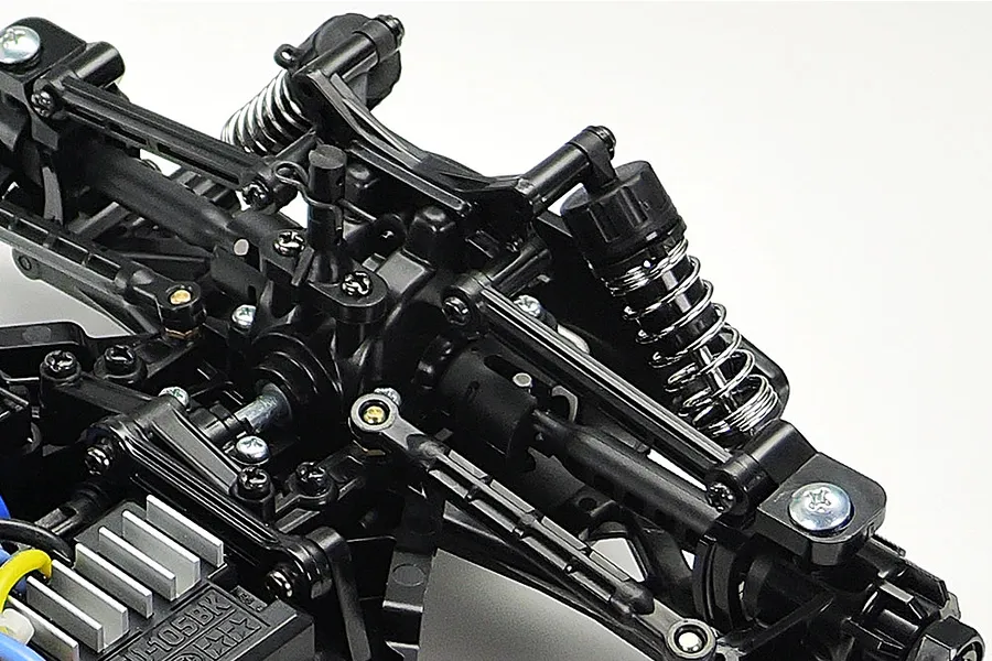 Close-up of the Tamiya TT-02B chassis suspension and drivetrain components, showing black plastic arms, coil-over shocks, and metal screws.