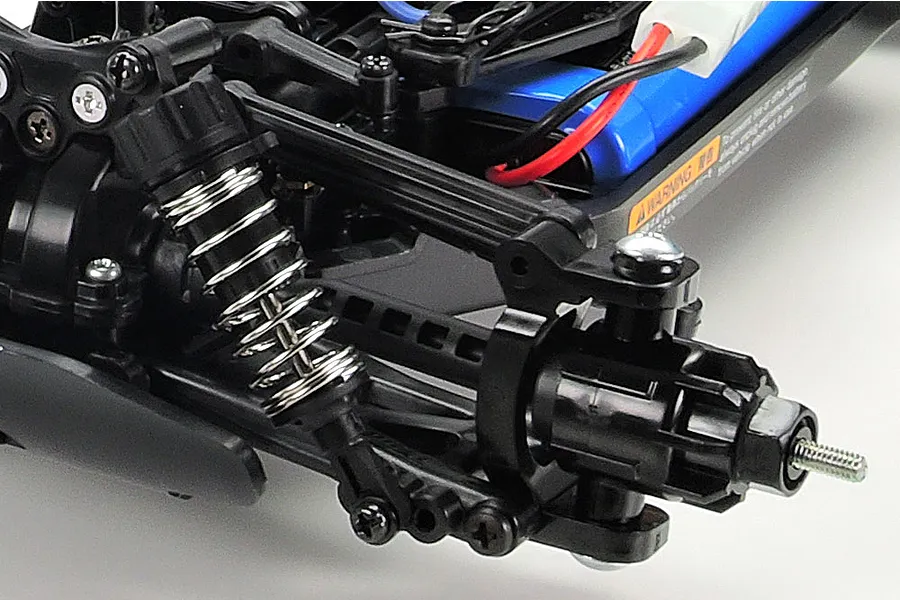 Close-up of the front suspension and wheel hub assembly on a Tamiya TT-02B RC buggy chassis, showing the coil-over shock and plastic suspension arms.