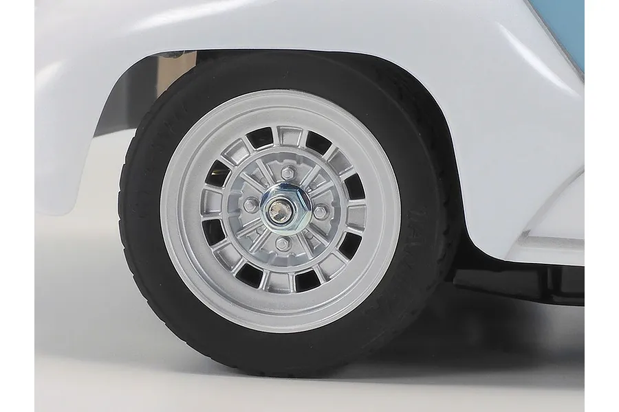 Close-up of the wheel and fender of a Tamiya Fiat Abarth 1000TCR RC car, showing the silver multi-spoke wheel and black rubber tire.