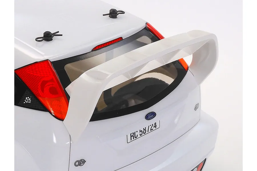 Close-up of the rear of a white Tamiya 2003 Ford Focus RS RC car body, showing the large rear spoiler, taillights, and body clips on a white background.