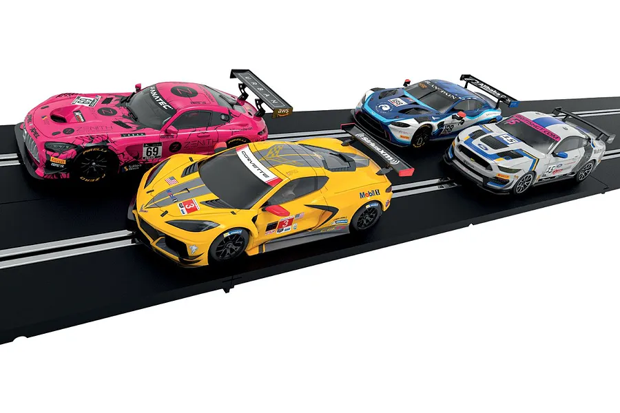 Four Scalextric 1/32 scale slot cars in pink, yellow, blue, and white racing liveries positioned on a black plastic slot car track.