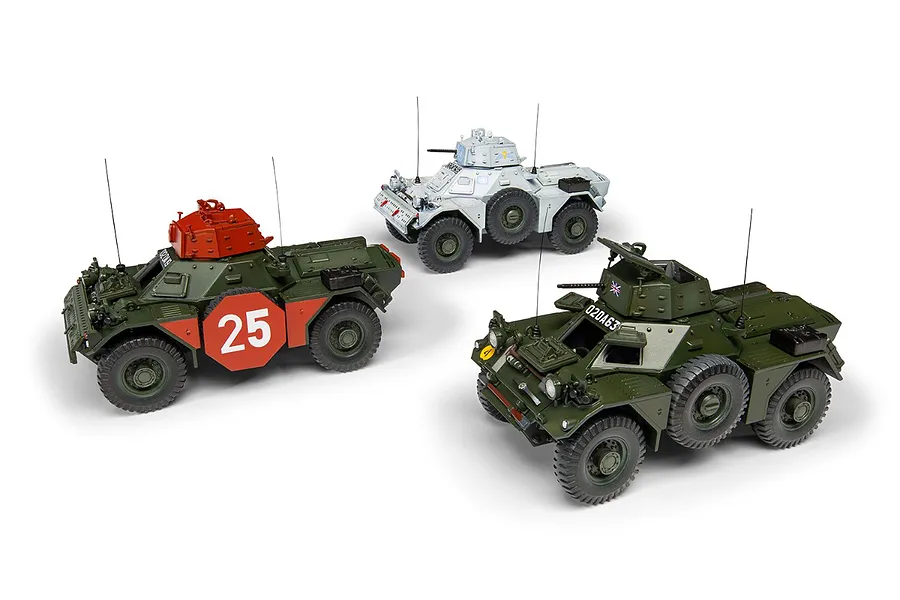 Three assembled and painted plastic model Ferret Scout Car MK.2 vehicles in different camouflage schemes on a white background.