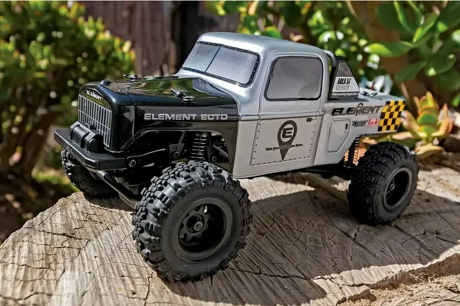 A silver and black Element RC Enduro24 Ecto 1/24 scale RC rock crawler parked on a wooden log outdoors.