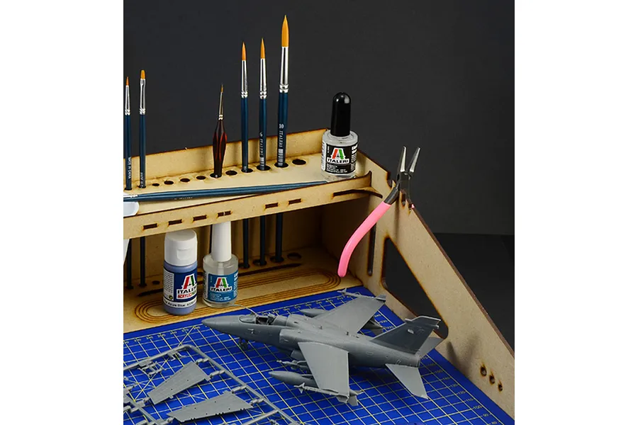 A wooden Italeri modelling workstation with a blue cutting mat, holding various paint brushes, glue, and a model aircraft kit.