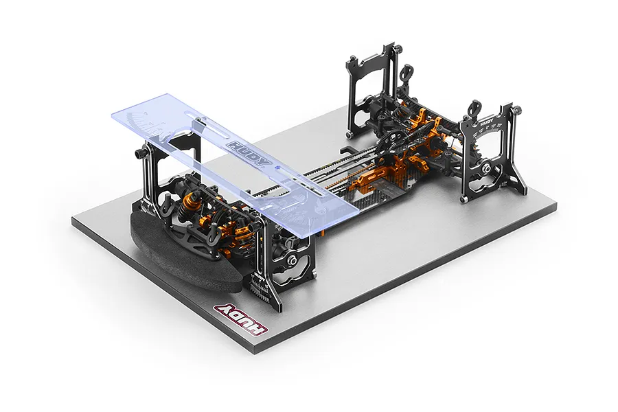 A Hudy 1/10 scale universal set-up station mounted on a grey base plate, featuring black and orange anodized aluminium components and a clear acrylic gauge.