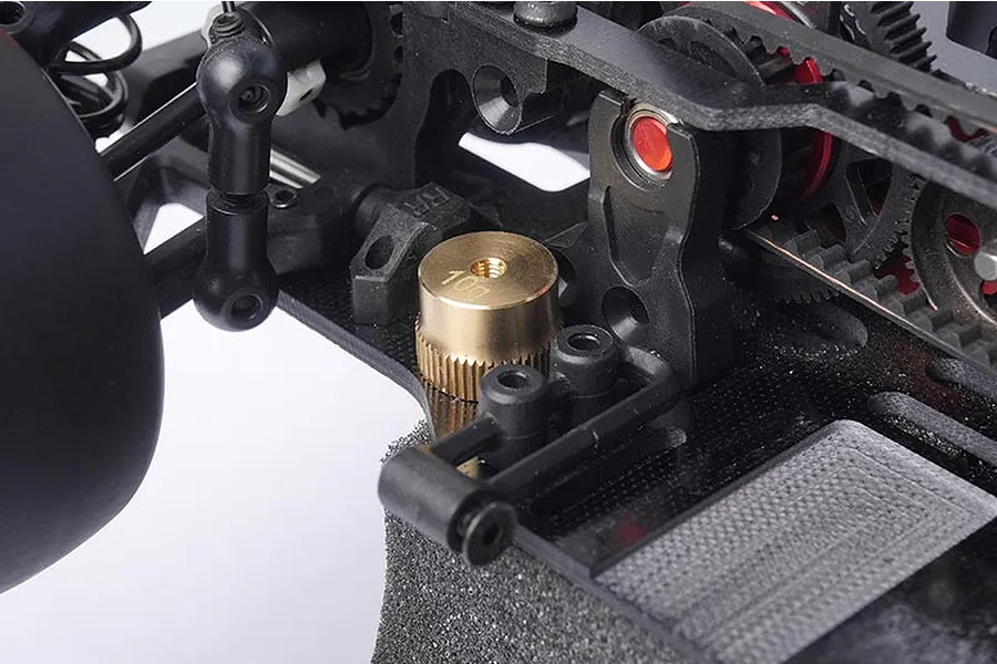 A close-up view of a 10g brass weight installed on the chassis of an RC car, showing the threaded top and knurled sides.