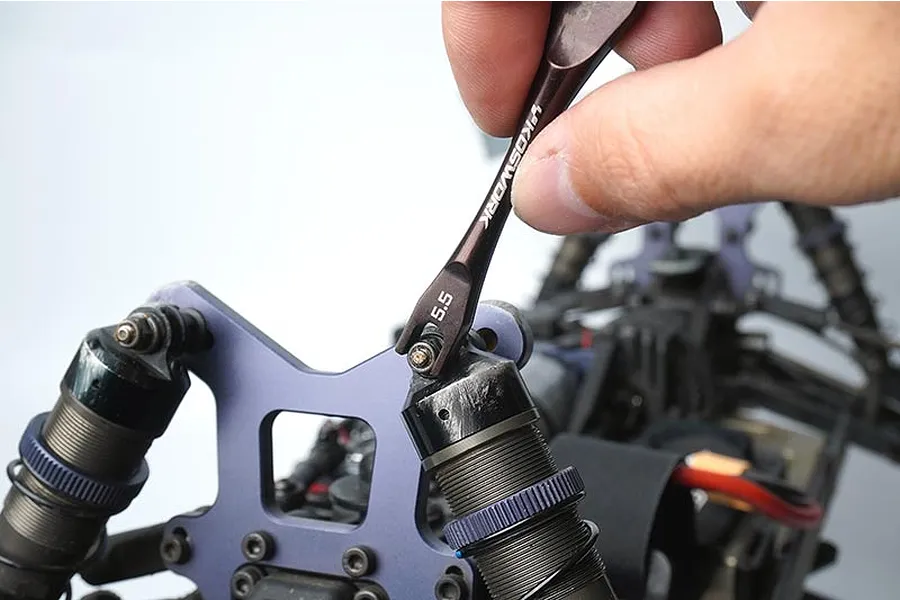 A hand using a Koswork 5.5mm turnbuckle wrench on the shock tower of an RC car.