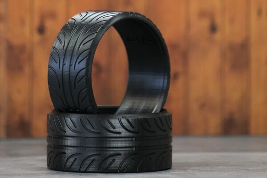Two black Pandora RC 2-inch ultra-flat display tires stacked on a grey surface against a wooden background.