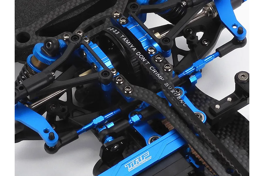 Close-up of the blue anodized aluminum and carbon fiber chassis components of a Tamiya TRF421 RC touring car kit.