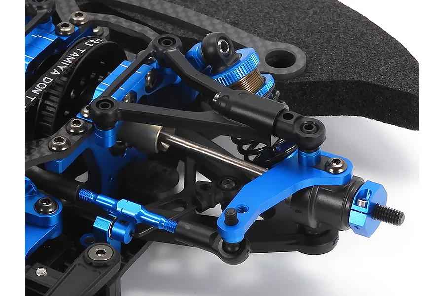 Close-up of the blue anodized aluminum front suspension and steering assembly on a Tamiya TRF421 RC touring car chassis.