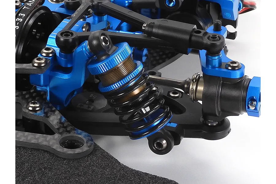 Close-up of the front suspension assembly on a Tamiya TRF421 RC touring car, featuring blue anodized aluminum parts and carbon fiber components.
