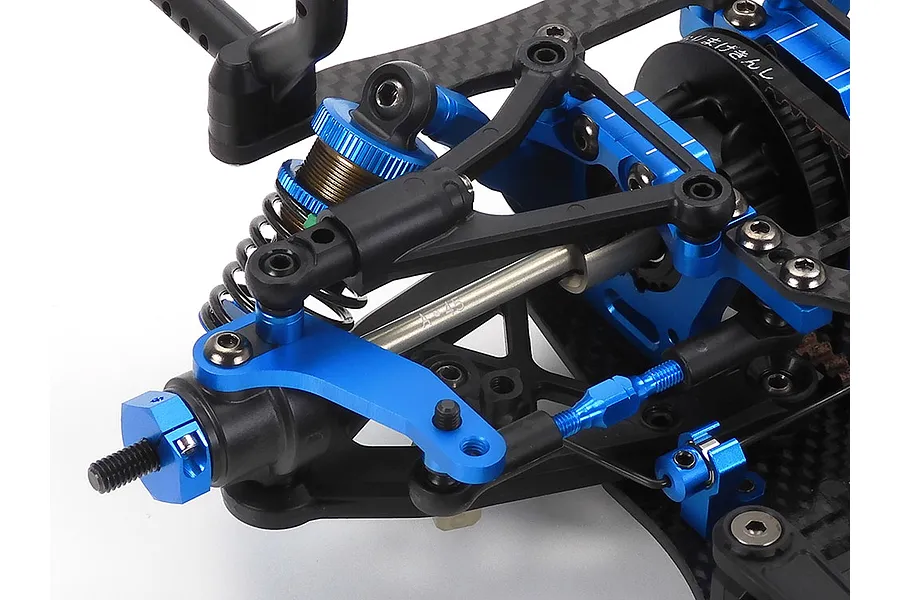 Close-up of the front suspension and steering assembly on a Tamiya TRF421 RC touring car, featuring blue anodized aluminum parts and carbon fiber chassis.