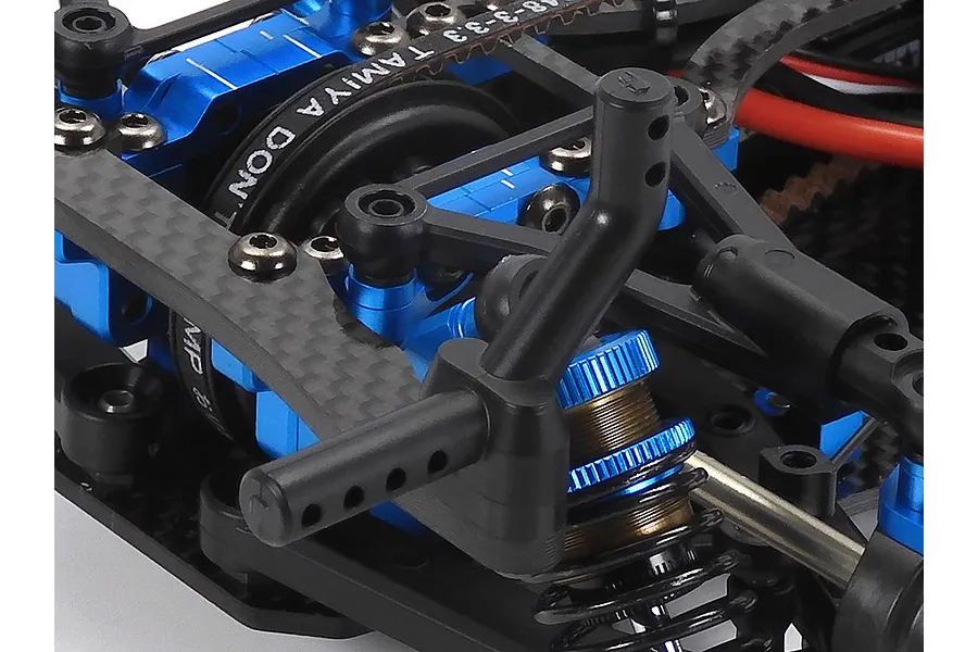 Close-up of the Tamiya TRF421 RC car chassis showing blue anodized aluminum suspension parts, carbon fiber shock tower, and black plastic body post.