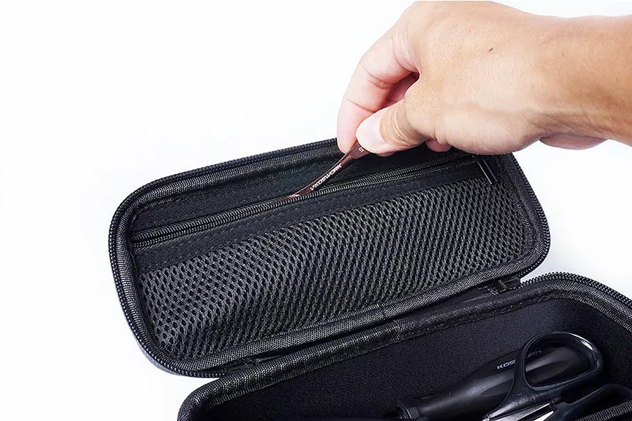 A hand placing a small metal tool into the zippered mesh pocket inside a black Koswork hard case.