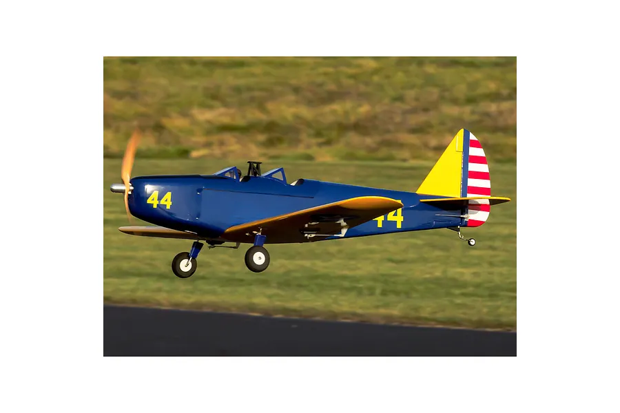 A blue and yellow Hangar 9 PT-19 RC warbird plane in flight over a grassy field with the number 44 visible on the fuselage.