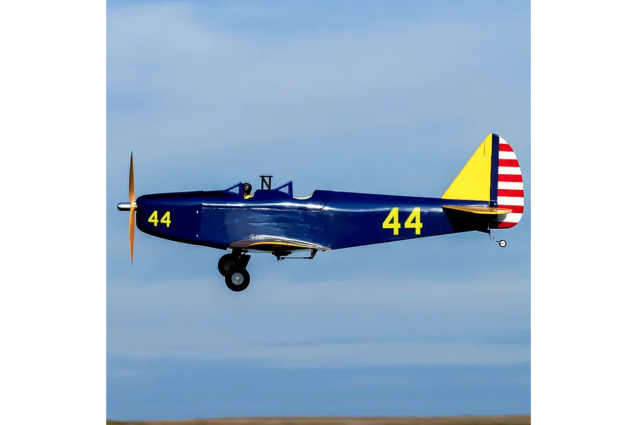 A Hangar 9 PT-19 RC plane in flight against a blue sky, featuring a dark blue fuselage with yellow accents and the number 44 on the side.