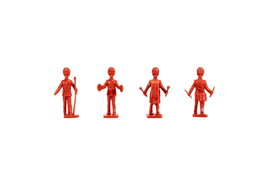 Four unpainted red plastic model figures of British Guards band members standing in a row against a white background.