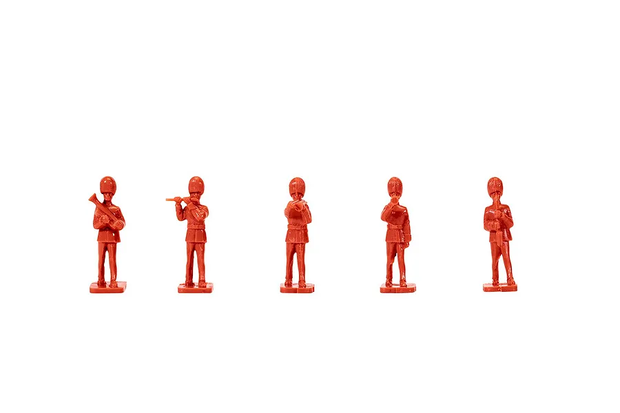 Five unpainted red plastic model figures of British Guards band members standing in a row against a white background.