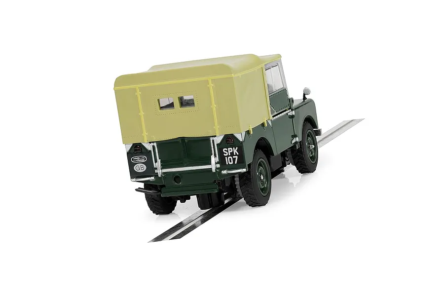 Rear three-quarter view of a green Scalextric 1/32 scale Land Rover Series 1 slot car with a tan canvas roof, positioned on a slot car track section.