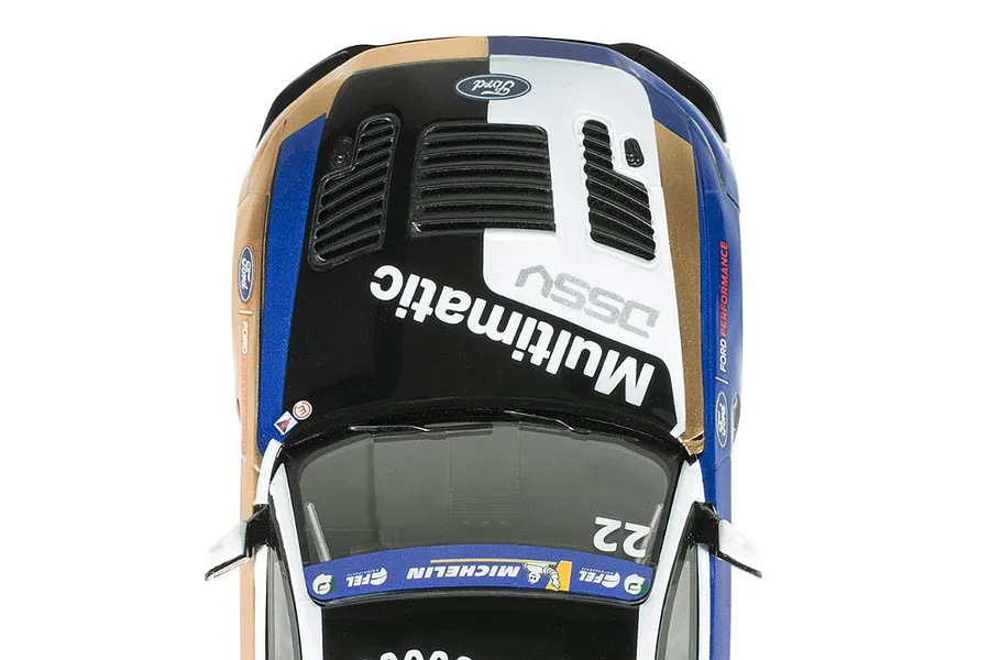 Top-down view of a Scalextric 1/32 Ford Mustang GT4 slot car featuring a black, white, blue, and gold livery with Multimatic branding.