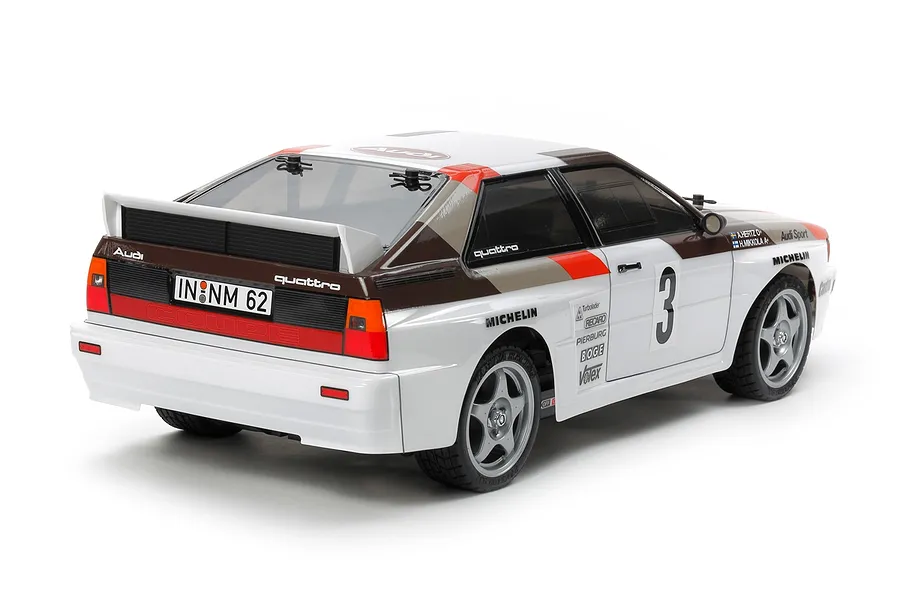 Rear three-quarter view of a Tamiya Audi Quattro A2 RC car model with white, brown, and red rally livery on a white background.